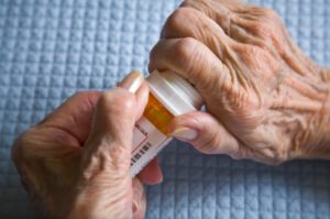 An image of the hands of an elderly person trying to unscrew a medicine bottle.